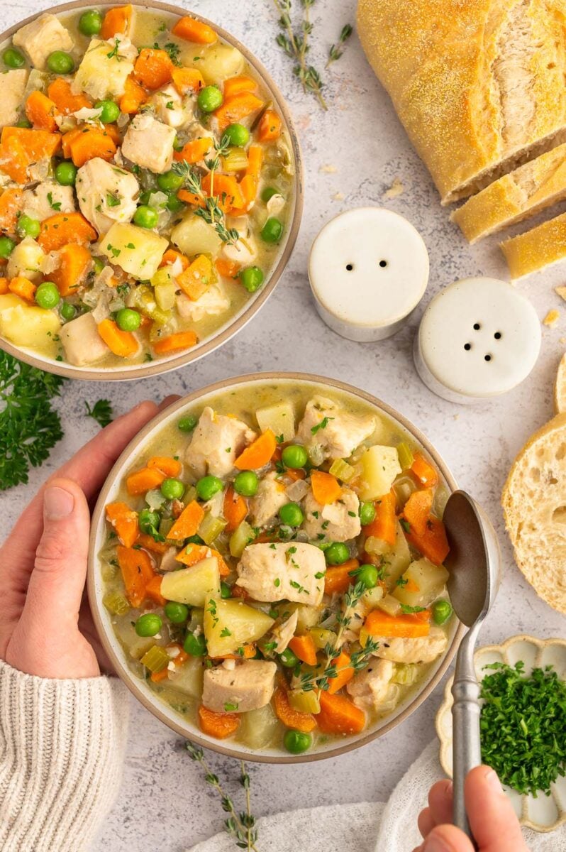 a big bowl of chicken stew with a hand taking a spoonful out