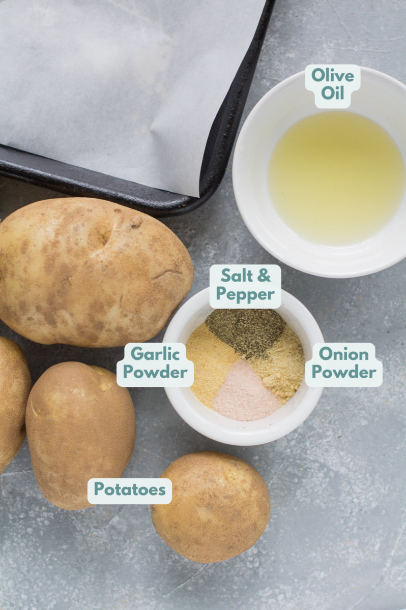 Ingredients for crispy roasted potatoes laid out on a grey background: olive oil, potatoes, salt and pepper, garlic powder (or minced garlic), onion powder
