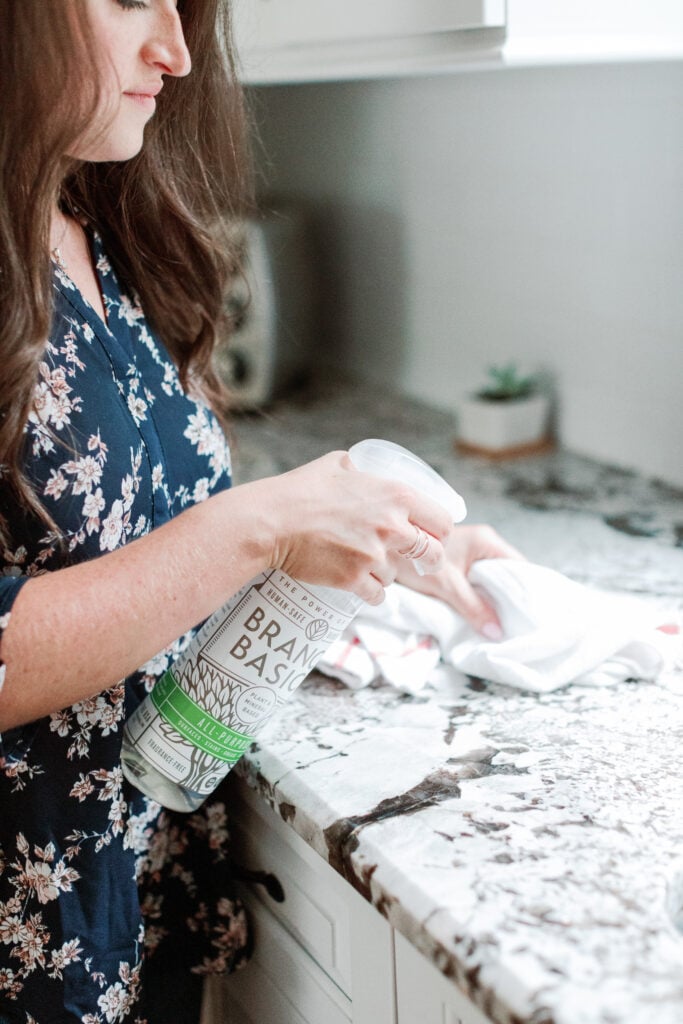 A girl spraying branch basics on a granite counter top