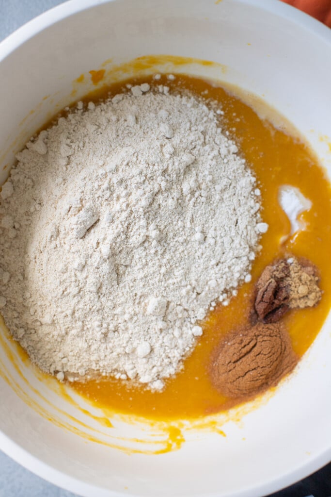 flour, baking powder, cinnamon, nutmeg and cloves being added into pumpkin muffin batter