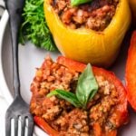 Whole30 stuffed peppers on a white plate with a grey background + green linen in the back.
