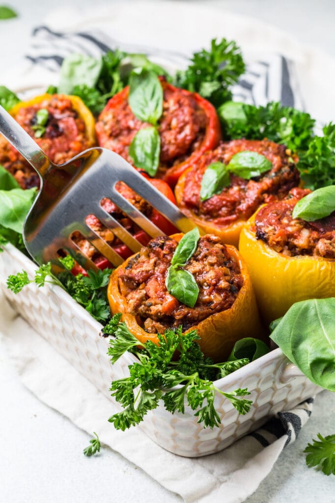 A large baking dish filled with whole30 stuffed peppers, a spatula scoops one serving out.