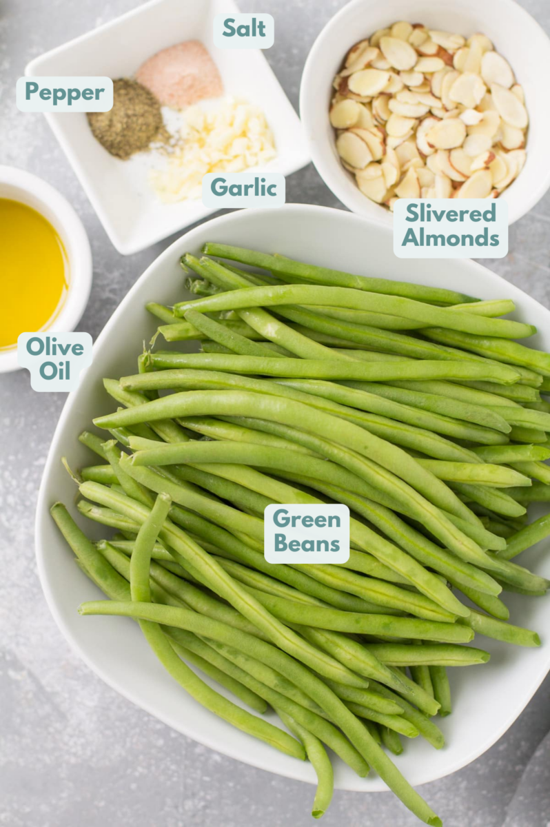 Ingredients for green beans almondine laid out on a grey background in small white bowls