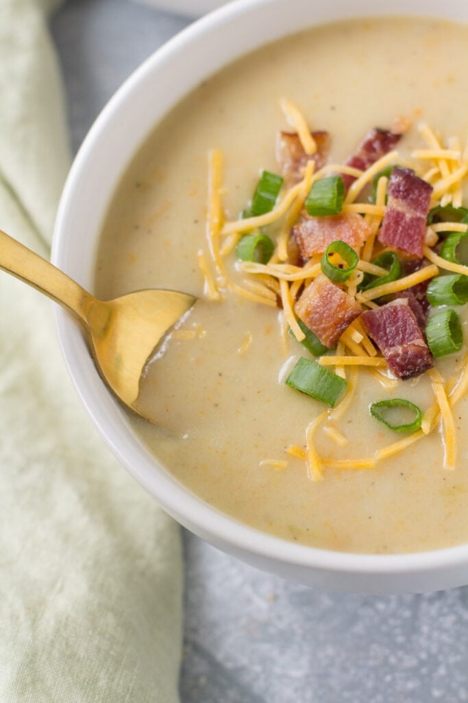 A bowl of healthy potato soup with a gold spoon taking a spoonful out