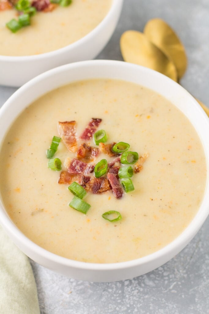 A close up image of healthy potato soup in a white bowl topped with bacon and chives