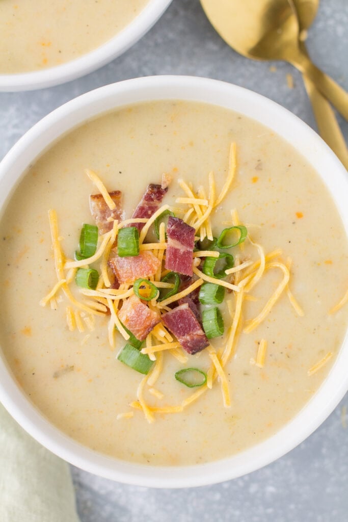 An overhead, close up image of whole30 paleo potato soup with bacon, cheese and chives. Gold spoons are stacked in the top left corner.