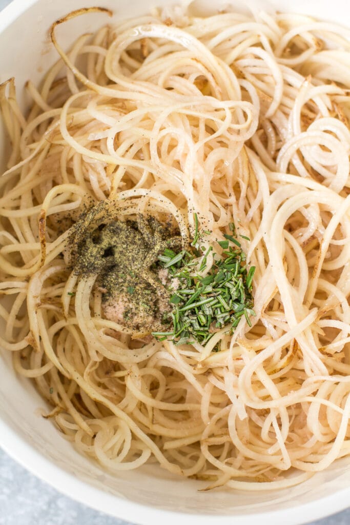 A close up of spiralized potatoes with rosemary and pepper