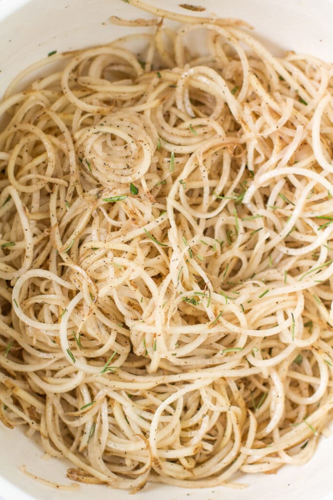 spiralized potatoes being tossed in a large white bowl
