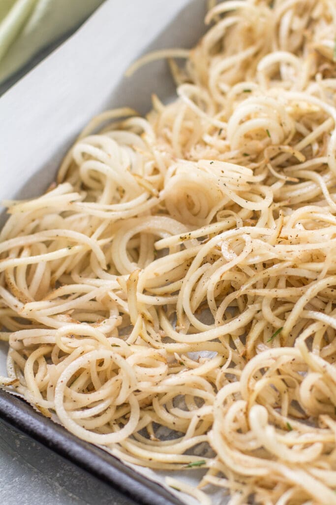 spiralized potatoes on a parchment lined sheet before going in the oven