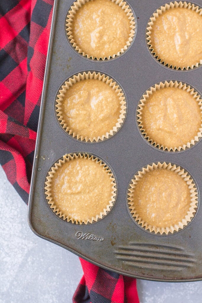 An overhead image of gingerbread muffins before being baked in a muffin pan on a grey background
