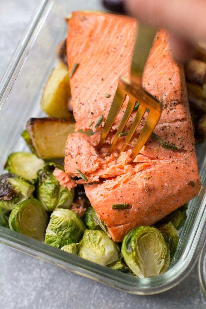 A fork taking a bite out of lemon salmon in a glass container