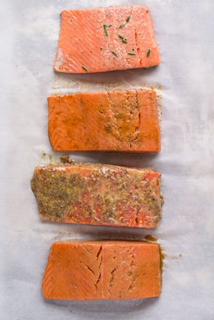 a close up of healthy salmon baking on a parchment lined baking sheet
