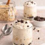 Healthy Almond Joy Overnight Oats in a clear glass jar with almonds and mini chocolate chips scattered around and on top with another jar in the background.