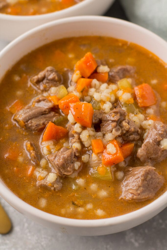 A close up of beef barley soup in a white bowl