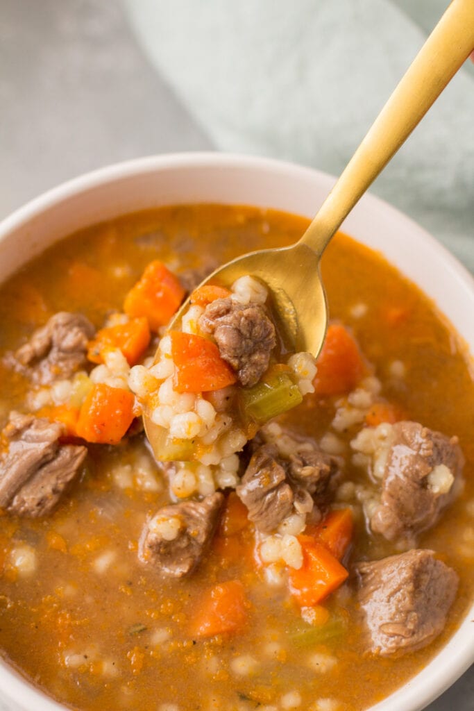 A spoon taking a scoop out of beef barley soup