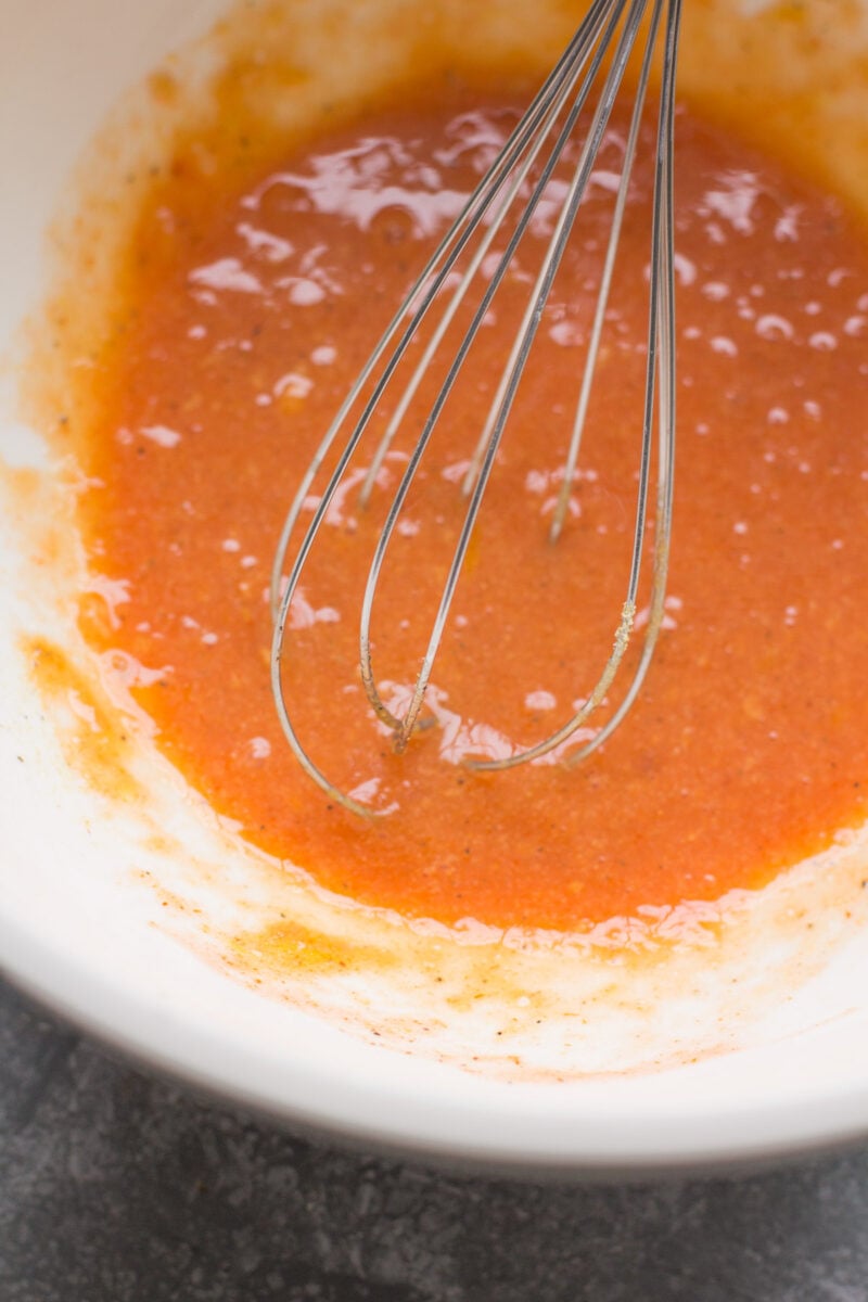 Eggs, olive oil, spices + buffalo sauce being whisked together in a bowl.
