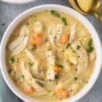 Healthy Chicken Pot Pie Soup in a white bowl on a grey background. Gold spoons are off to the right side