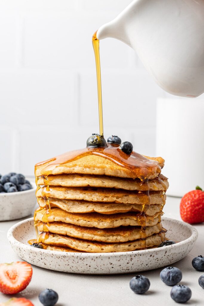 Maple syrup being poured on healthy pancakes