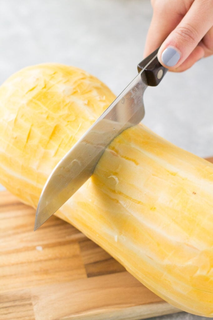 Butternut squash being cut on a wooden cutting board
