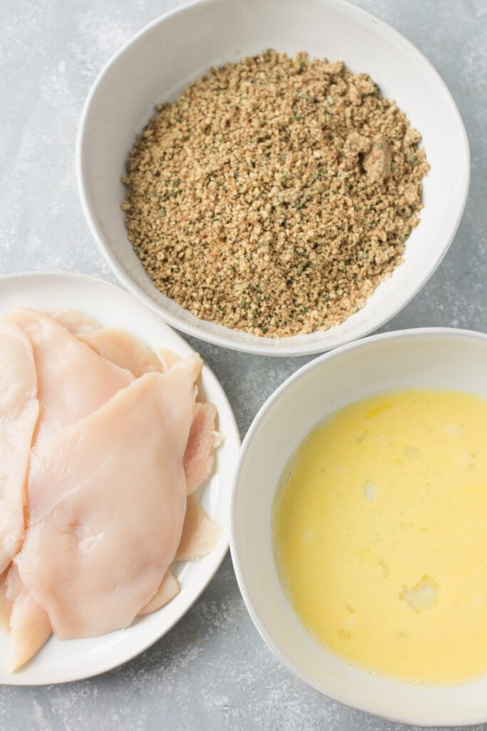 Bowls for pecan chicken cutlet breading set aside. a bowl of chicken cutlets, a bowl of egg mix and a bowl of breading