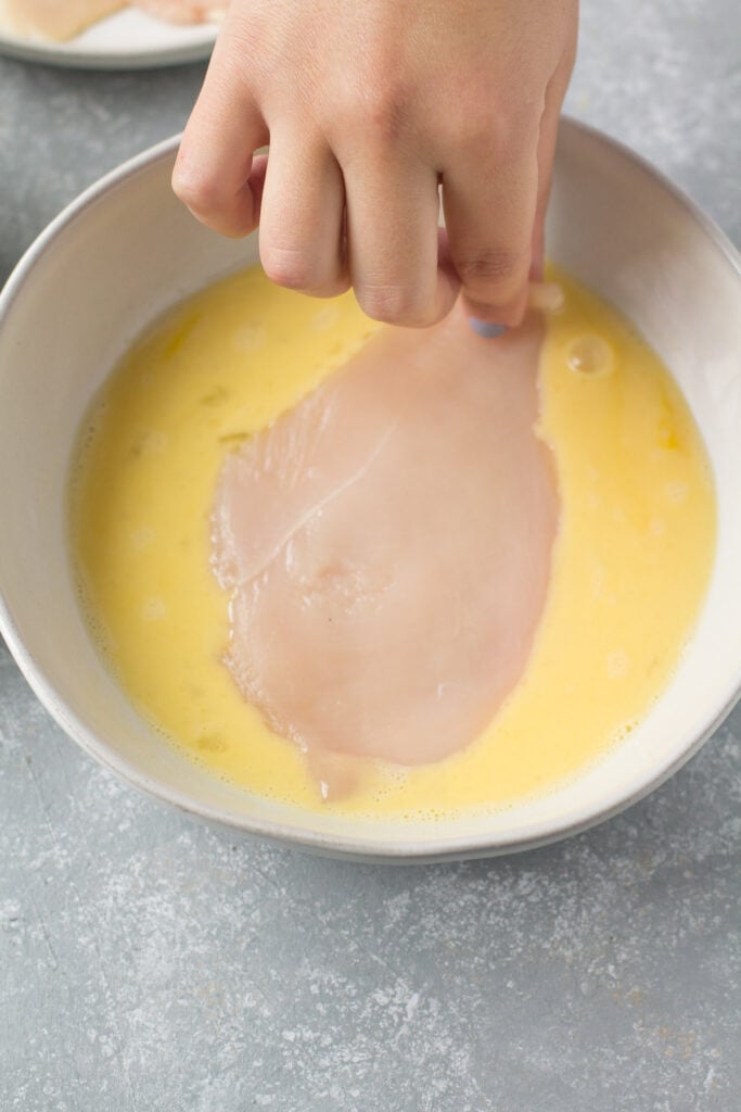 a chicken cutlet being dipped into an egg batter