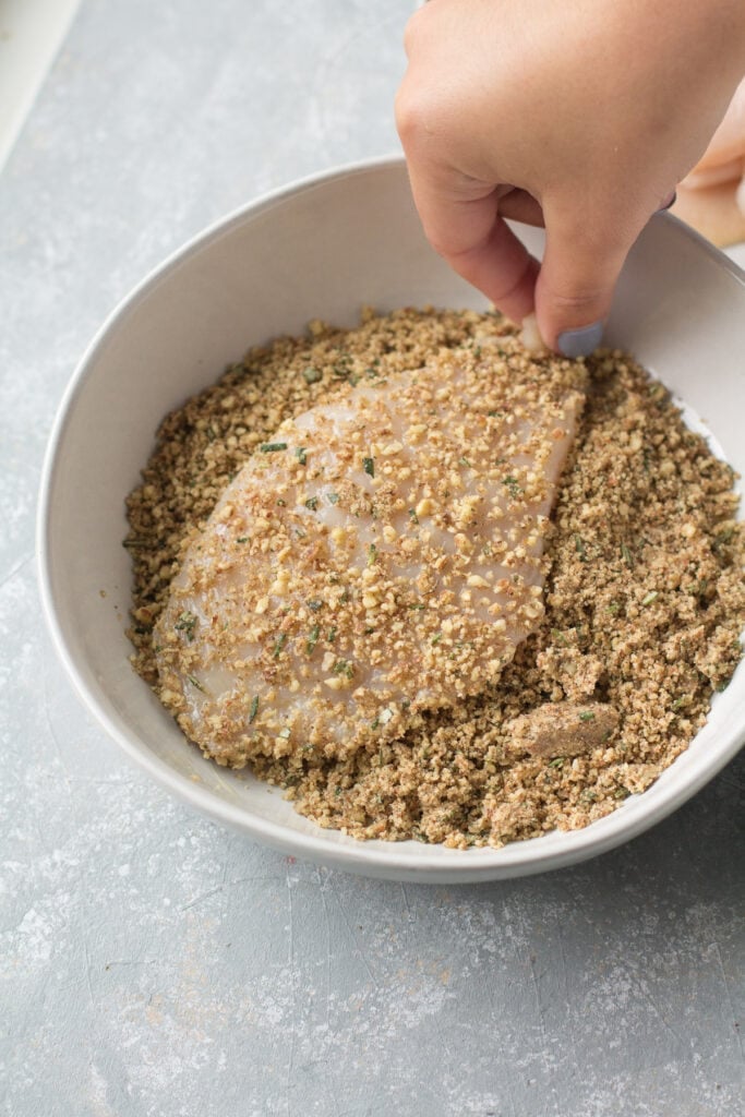 a chicken cutlet being dipped into pecan breading