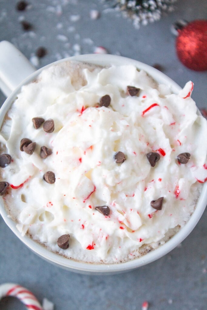 A close up of a peppermint mocha on a grey background with candy canes and ornaments off to the side