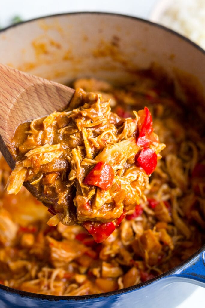 Whole30 Slow Cooker Fall Chicken Chili in a blue dutch oven with a wooden spoon stirring it.