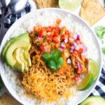 Pumpkin Chicken Chili in a white bowl topped with cheese, tomatoes, limes and avocado