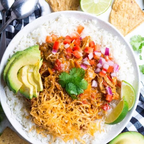 Pumpkin Chicken Chili in a white bowl topped with cheese, tomatoes, limes and avocado
