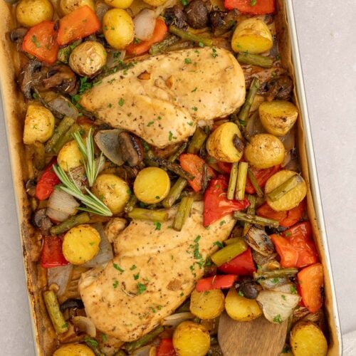 Sheet Pan Balsamic Chicken and Veggies on a parchment lined baking sheet with a wooden spoon in it.