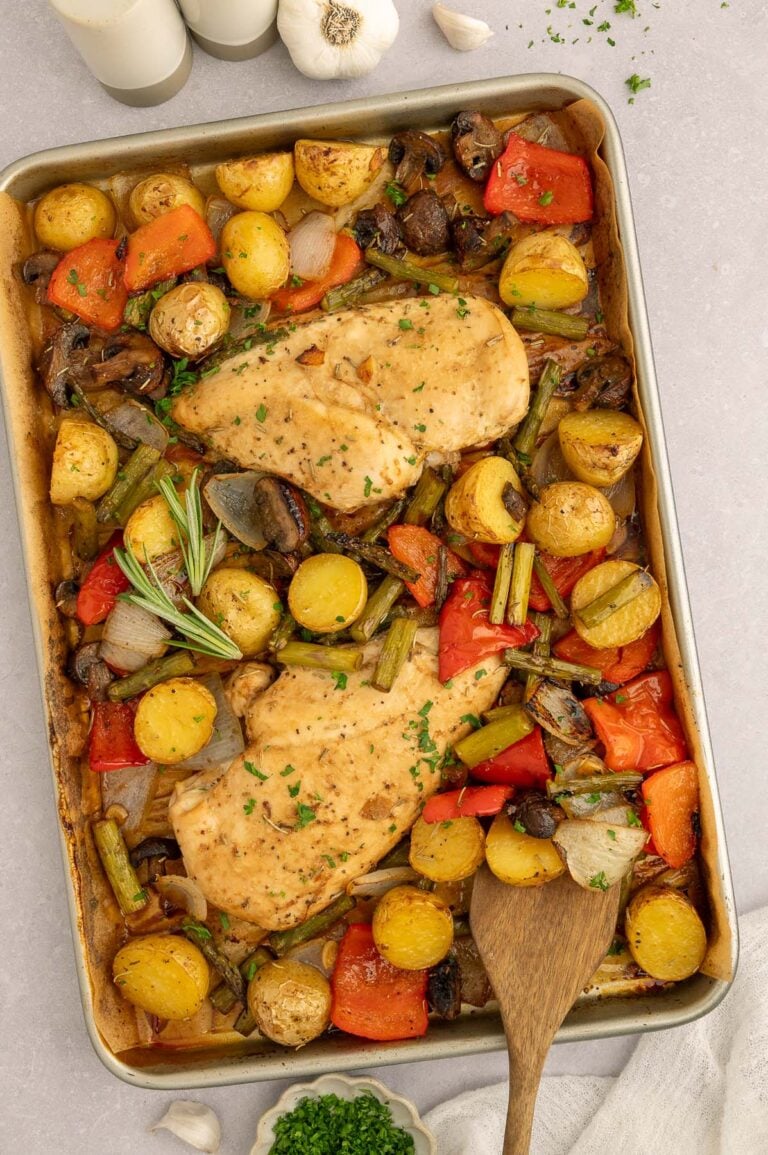 Sheet Pan Balsamic Chicken and Veggies on a parchment lined baking sheet with a wooden spoon in it.