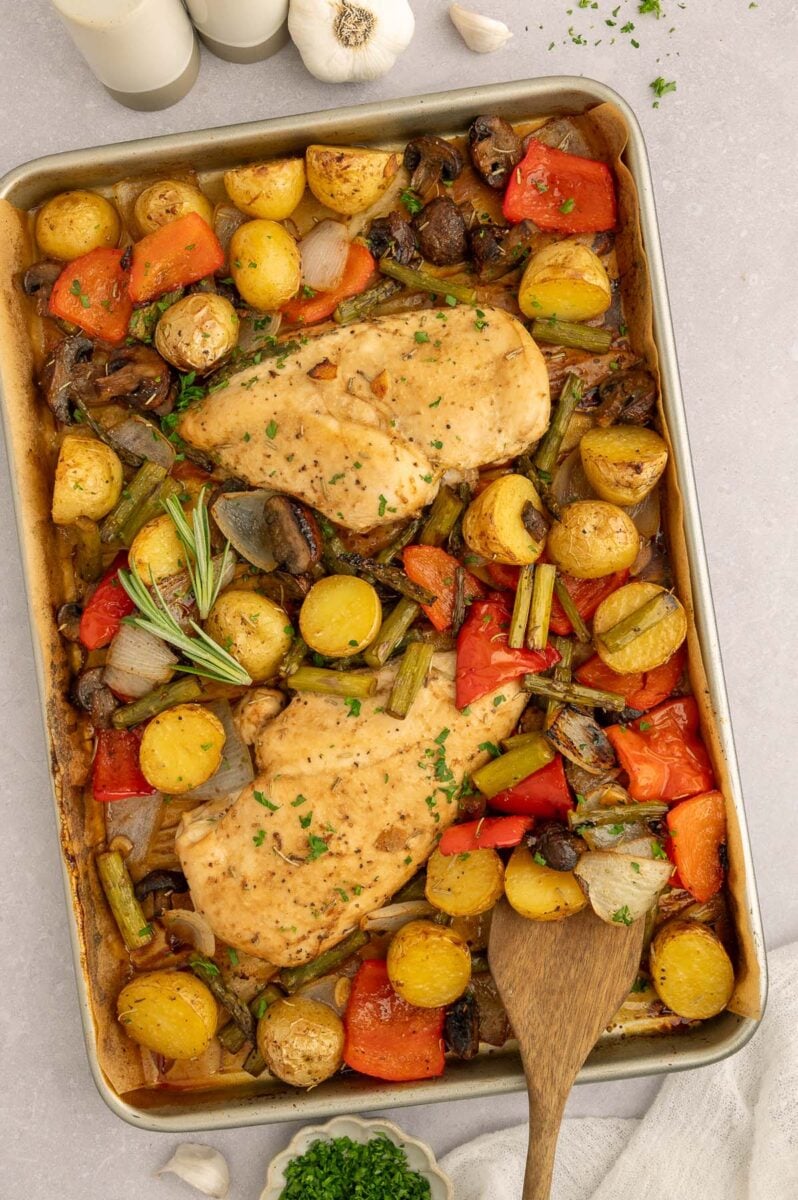 Sheet Pan Balsamic Chicken and Veggies on a parchment lined baking sheet with a wooden spoon in it.
