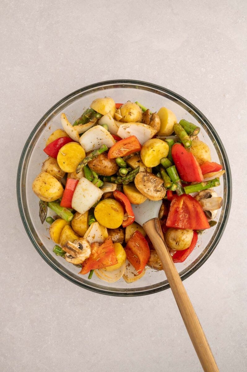 Uncooked veggies in a bowl with a wooden spoon after tossing with a balsamic marinade.