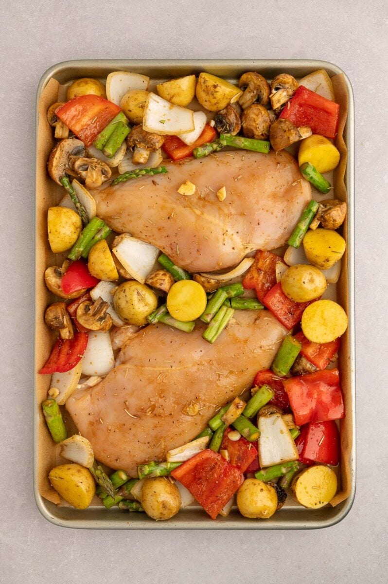 Uncooked Sheet Pan Balsamic Chicken and Veggies on a parchment lined baking sheet ready to go in the oven.