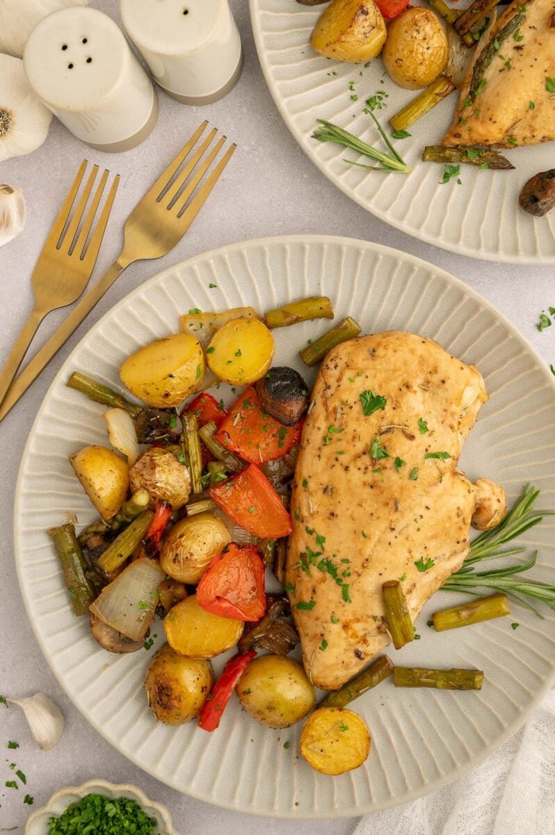 A plate of sheet pan balsamic chicken and veggies with another plate and gold forks on the side.
