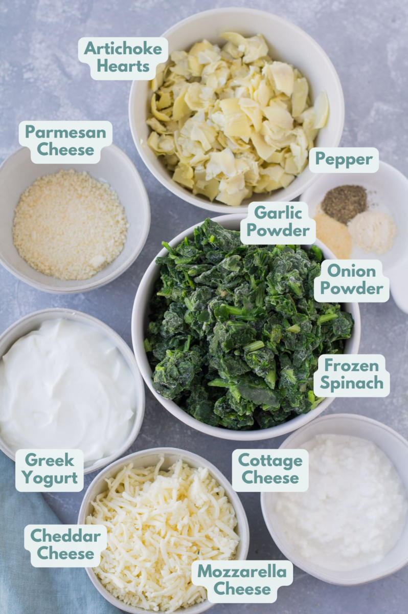 ingredients for healthy spinach artichoke dip laid out in small white bowls on a grey background.