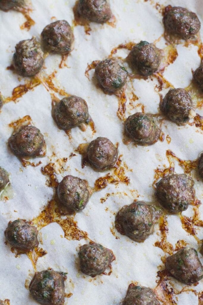 An overhead image of baby meatballs for italian wedding soup on a parchment lined baking sheet