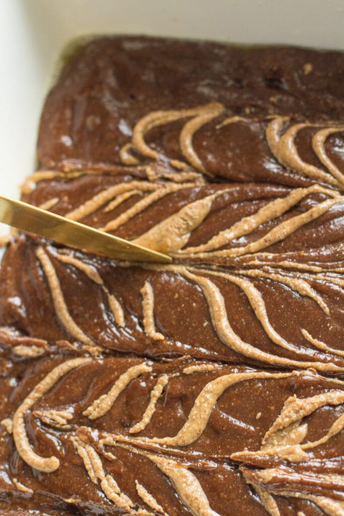 a close up of almond butter brownies with almond butter being swirled into the top