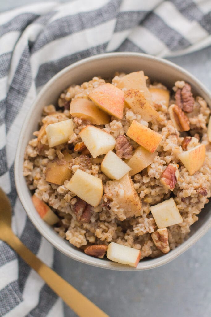 Baked Oatmeal made with steel cut oats with apples and pecans in a small white bowl on a grey background