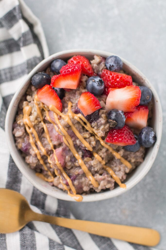 A close up of baked steel cut oatmeal with berries in a small white bowl with a gold spoon off to the side.
