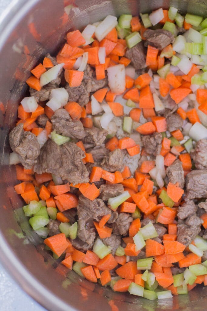 Beef barley soup sauteing in an instant pot with large chunks of beef stew meat