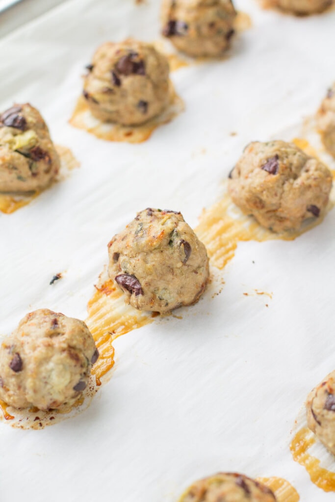 A baking sheet with baked greek turkey meatballs fresh out of the oven