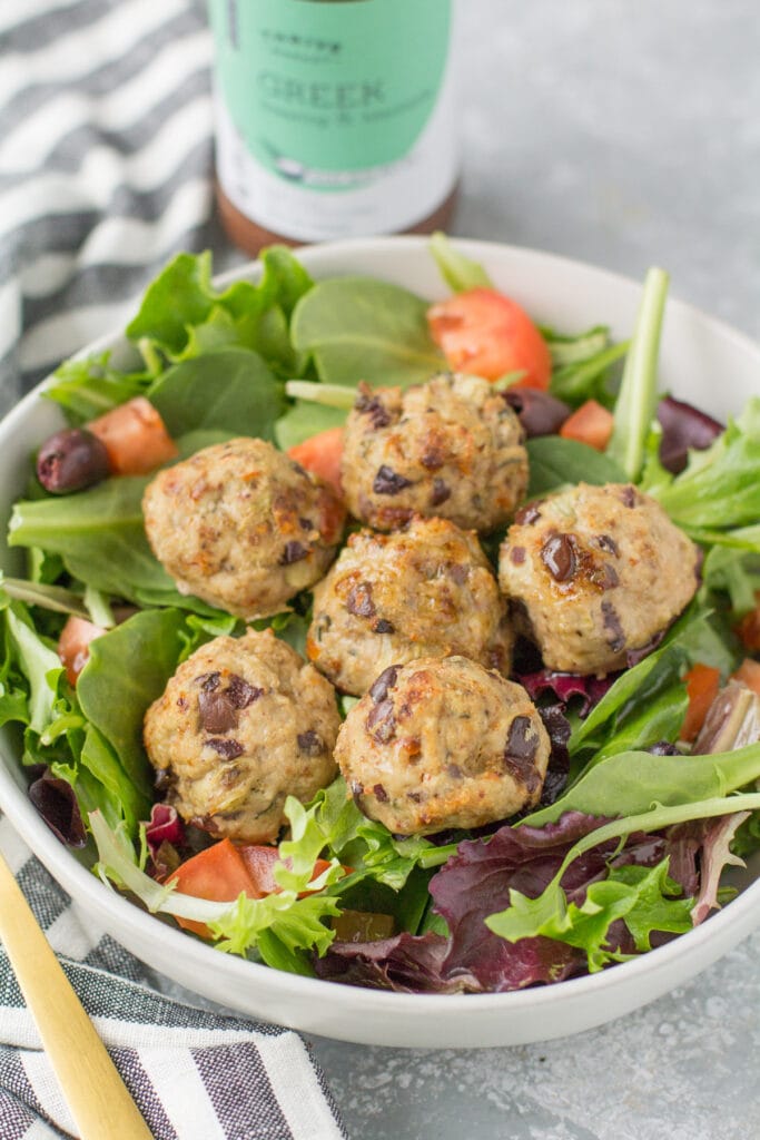Greek meatballs on a salad on a grey background. with a bottle of dressing in the back.