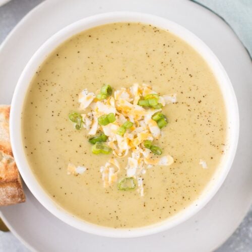 An overhead shot of Healthy Broccoli Soup in a white bowl on a white plate with bread off to the side.