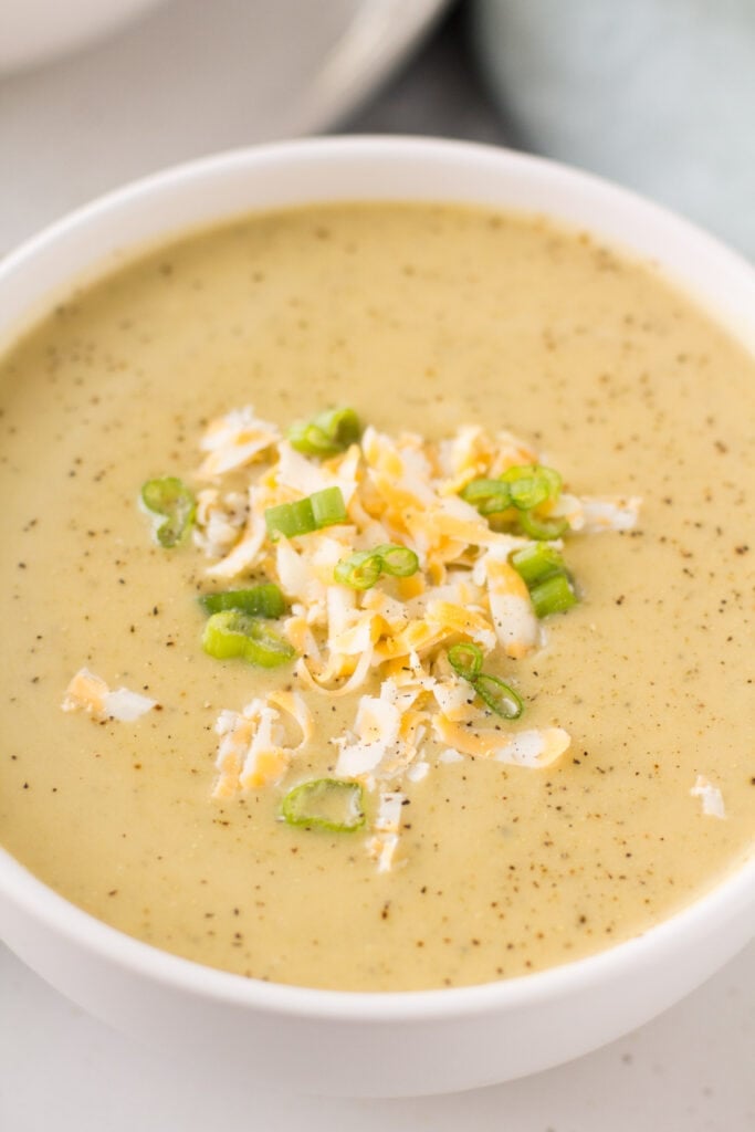 A close up of healthy broccoli cheddar soup in a white bowl with another bowl in the background
