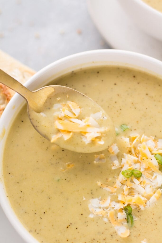 A close up image of a spoon taking a scoop out of a bowl of healthy broccoli cheddar soup