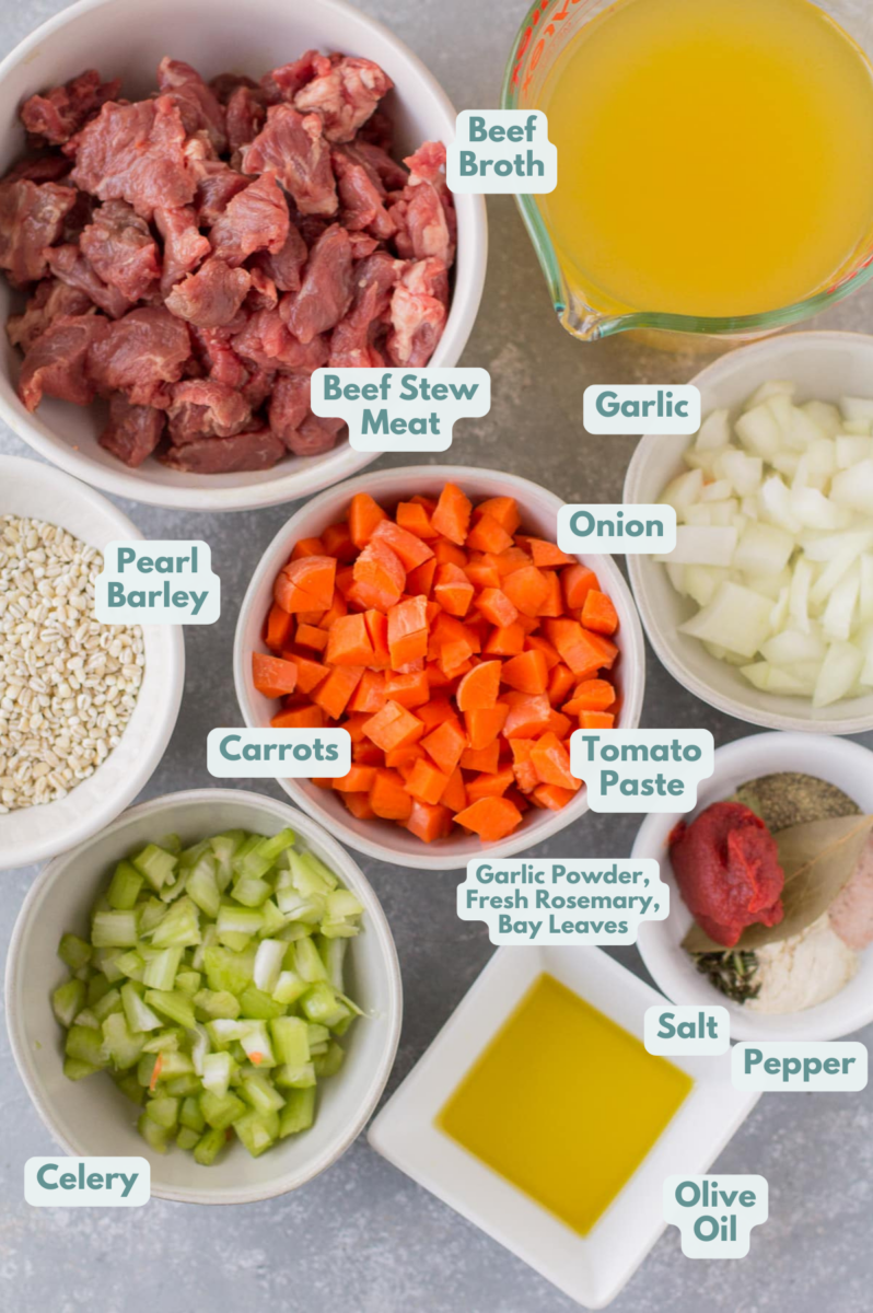 ingredients for beef barley soup in small bowls on a grey background: beef stew meat, extra virgin olive oil, salt and pepper, garlic powder, fresh rosemary, bay leaves, beef broth, pearl barley, veggies, tomato paste, parmesan cheese rind (optional)