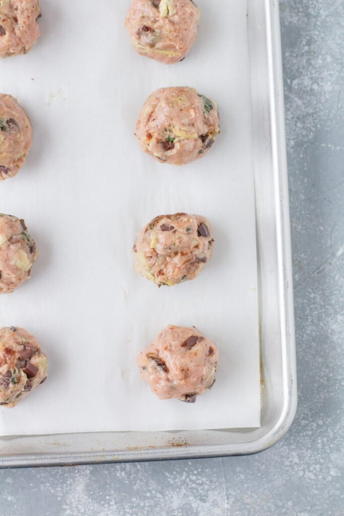 greek meatballs rolled out and placed on a parchment lined baking sheet