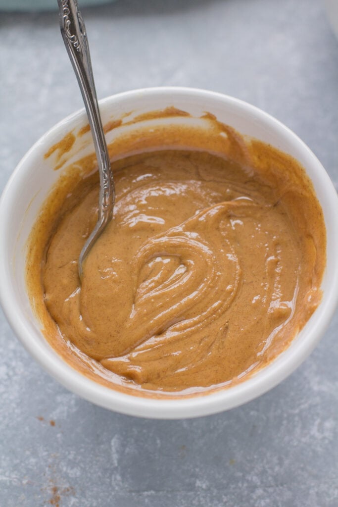 a close up of peanut butter granola batter being mixed in a small white bowl